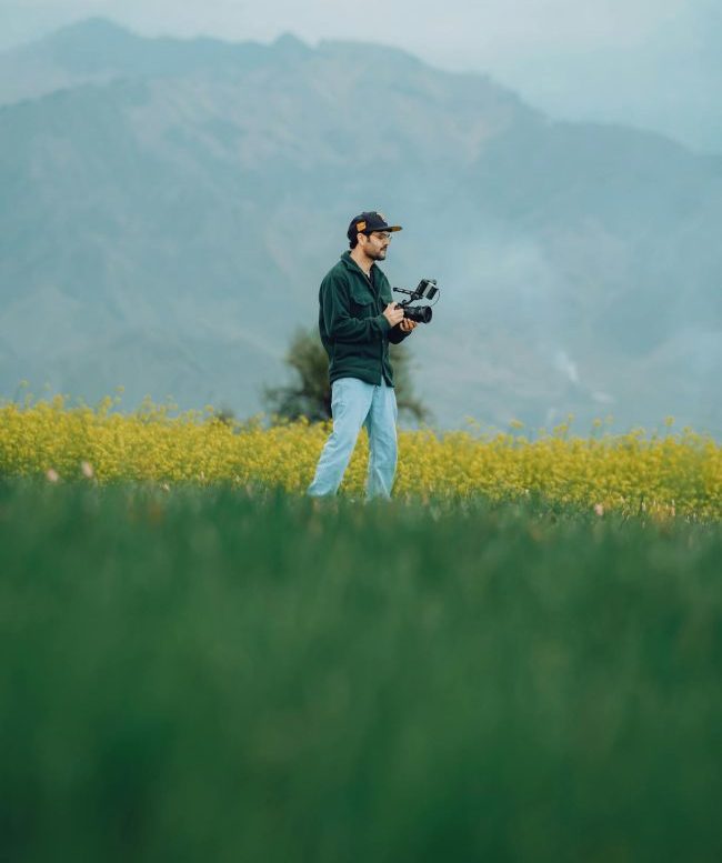 Man Standing with Camera on Meadow with Flowers